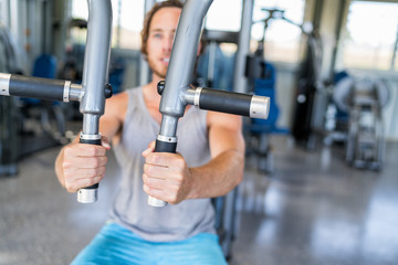 Gym machine closeup on male hands. Male athlete training chest muscles on fitness equipment pec deck fly working out strength alone indoors. Man holding handles of fitness machine at gym center.