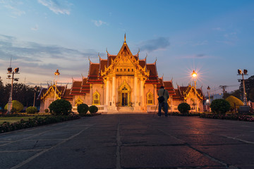 Man standing shooting Wat Benchamabophit the Marble Temple, Bangkok at twilight