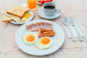Breakfast with Fried egg, Ham, Sausage, toast, jam, butter, water melon, orange juice and black coffee on marble table.