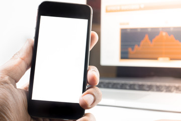 Hand holding Blank Screen of Smart phone with graph in laptop