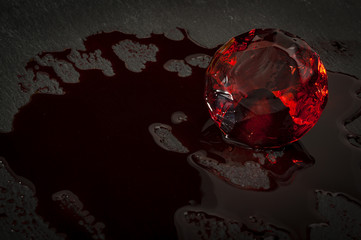 Blood diamond concept with a diamond covered in red blood in a dark setting resembling a mine with...