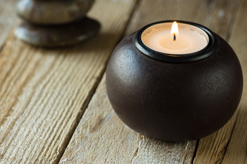 White tea light in a black wood candle holder and zen balanced stones in background,copyspace for text, harmony concept
