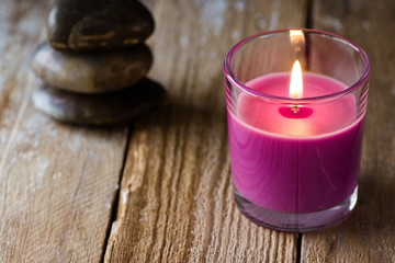Lilac lavender candle and a stack of balanced zen stones in the background, on wood surface, close up, copyspace for text, harmony concept