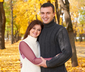 Fototapeta premium happy adult couple embrace in autumn city park, trees with yellow leaves, bright sun and happy emotions, tenderness and feelings