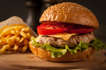 Home made hamburger with beef, onion, tomato, lettuce and cheese. Fresh burger closeup on wooden rustic table with potato fries, beer and chips.