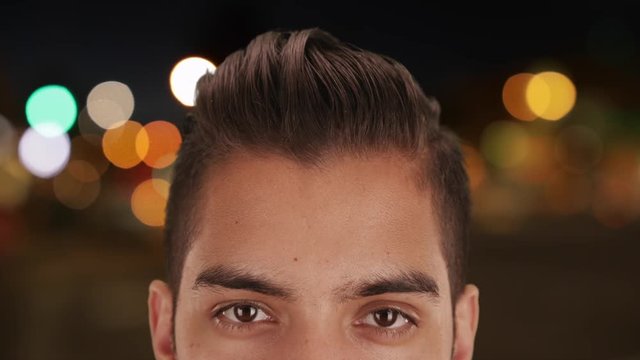 Close Up of young millennial man with undercut standing outside at night with lights and street out of focus in background. Cool handsome Hispanic guy with haircut