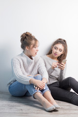 portrait two surprised girls looking at cell phone discussing latest gossip news, shopping, shocked at what they see, isolated white background