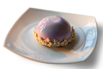 Small cake of pink color. Plate with glazed dessert. Blueberry mousse cake. Sugar and calories.