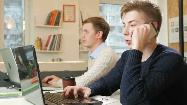 Young man working in the office of the laptops on the project. One is calling on the phone to the customer and records the answers. The concept of teamwork