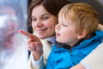 Cute little toddler boy and mother looking out train window making winter vacations