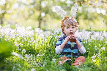 Cute happy little boy wearing Easter bunny ears and eating choco