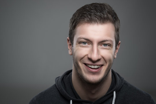 Close up moody portrait of young unshaven man smiling and looking at camera over gray background with copyspace