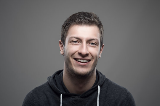 Young casual man wearing sporty hoodie smiling and looking at camera over gray background