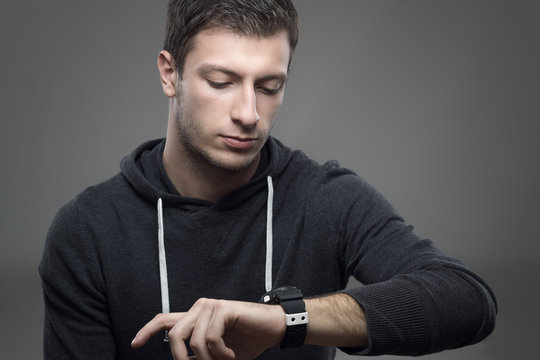 Sporty modern casual man in hoodie checking time on his wrist watch over gray background