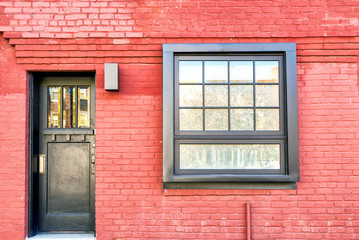 Red brick facade of apartment building with metal door and window