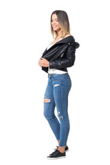 Obraz premium Pretty smiling shy casual girl wearing leather jacket, ripped jeans and black sneakers looking down. Full body length portrait isolated over white background