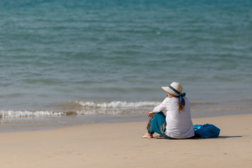 Fototapeta na wymiar Young woman sitting on a sandy beach and looking at a dark blue sea