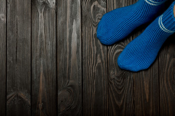 Legs knitted blue woolen socks on wooden dark background..