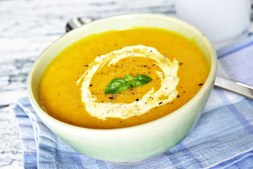 Bowl with pumpkin soup and cream on a wooden table.