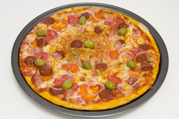 Pizza with chorizo, salami, bacon, onions and olives on a white wooden table, selective focus