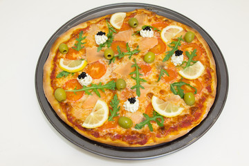 Pizza with salmon, olives, arugula and lemon on a white wooden table, selective focus