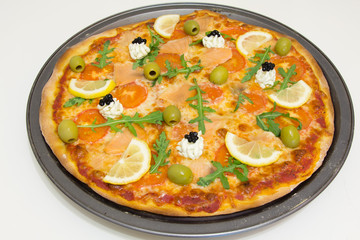 Pizza with salmon, olives, arugula and lemon on a white wooden table, selective focus