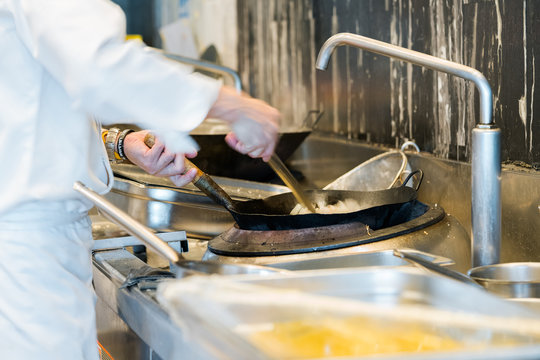 Chef cooking fried rice with flame in a frying pan on a kitchen stove, Chinese style
