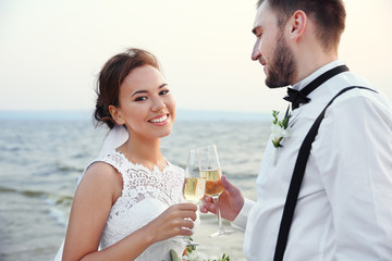Groom and bride with glasses of champagne on river bank