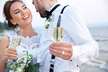 Groom and bride with glasses of champagne on river bank