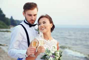 Groom and bride with glasses of champagne on river bank