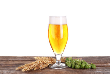 Glass of light beer, wheat spikelets and hop cones on wooden table, isolated on white