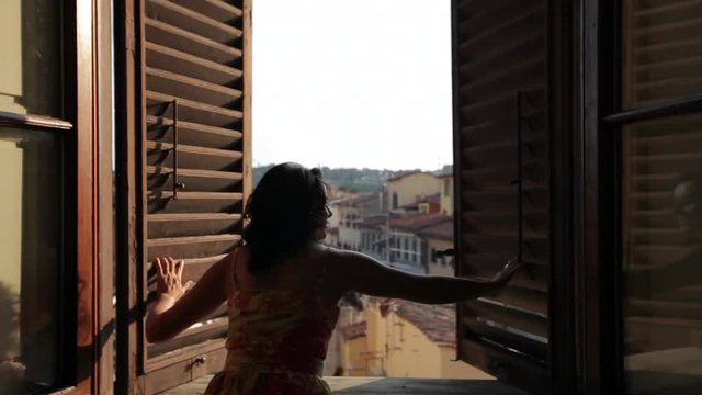 MH DS Woman Opening Windows Overlooking Old Town Rooftops / Florence, Italy