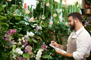 Handsome florist with notebook and pen in greenhouse