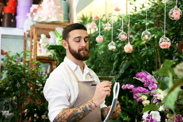 Handsome florist with notebook and pen in greenhouse