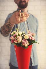 Tattooed man holding paper cone with beautiful bouquet, close up view