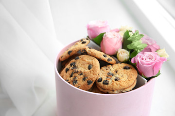 Box with beautiful flowers and cookies on light background, close up view