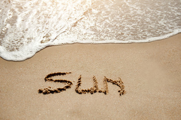 Sun written on the sand beach near sea - holiday relax concept
