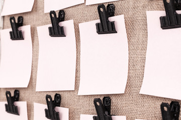 Notice board with clips holding blank square paper notes close up. Viewed at an angle
