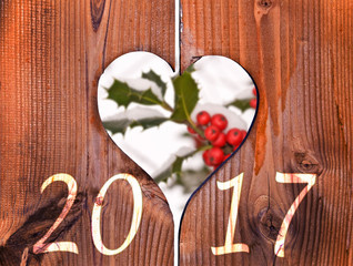 2017, wooden frame in the shape of a heart and branch of holly under the snow in the background