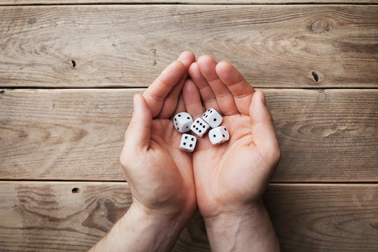 Man holding in hand white dice over the wooden table top view. Gambling devices. Game of chance concept.