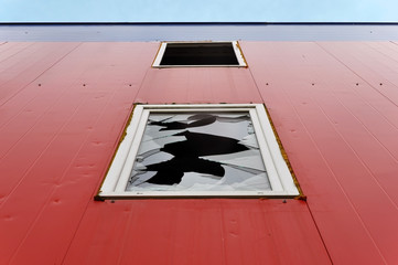 Abandoned industrial building. Red wall of sandwich-panels and a window with broken glass. Look up.