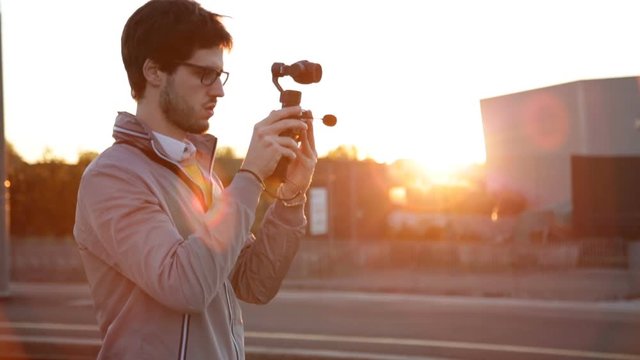 Young boy Glasses with a Grey Jacket is Taking a Video Footage with his modern Gimbal Camera Linked with his Smartphone.