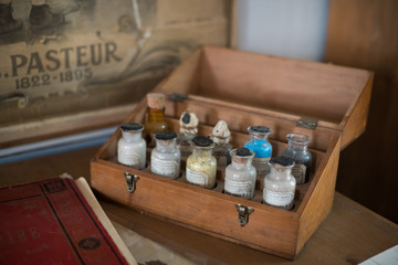 Old glass vials with products in a wooden box in front of a school wall