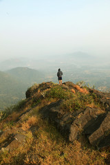 Young man standing on the top of a mountain and enjoying valley view