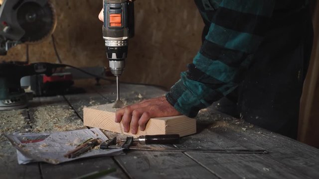of carpenter's hands using drill on wooden plank