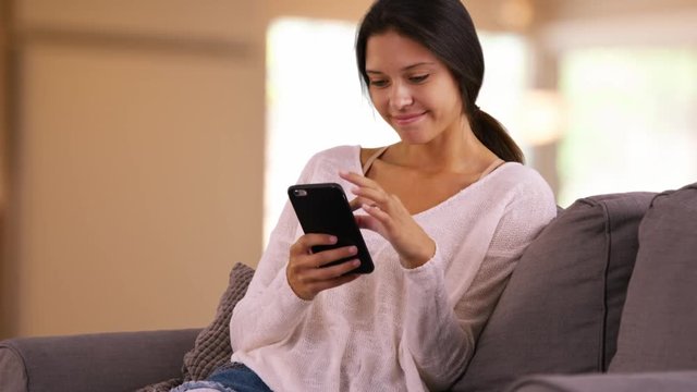 Young Caucasian woman uses her mobile phone to browse the internet. Millennial white girl uses her smart phone in her living room