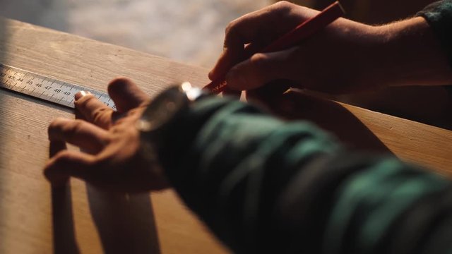 hand of a carpenter taking measurement of a wooden plank. sun flare ob background