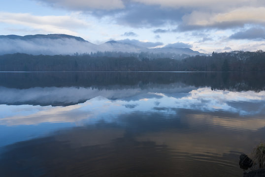 Mist and reflections on Loch Faskally caught in the sunlight under a veil of mist, Pitlochry, Scotland.