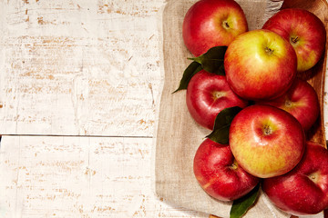 Fresh red apples with green leaves and linen napkin on rustic background. Free space for text. Top view