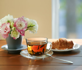 Cup of tea with croissant and flowers in vase on table